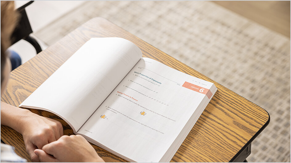 Student sits at a wooden desk with an open Eureka Math Squared workbook turned to a Lesson 6 page on properties of exponents.
