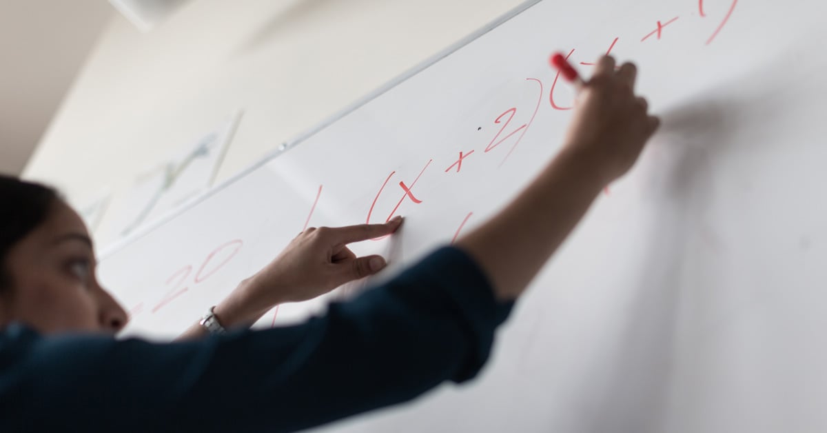 Teacher standing and writing on whiteboard.