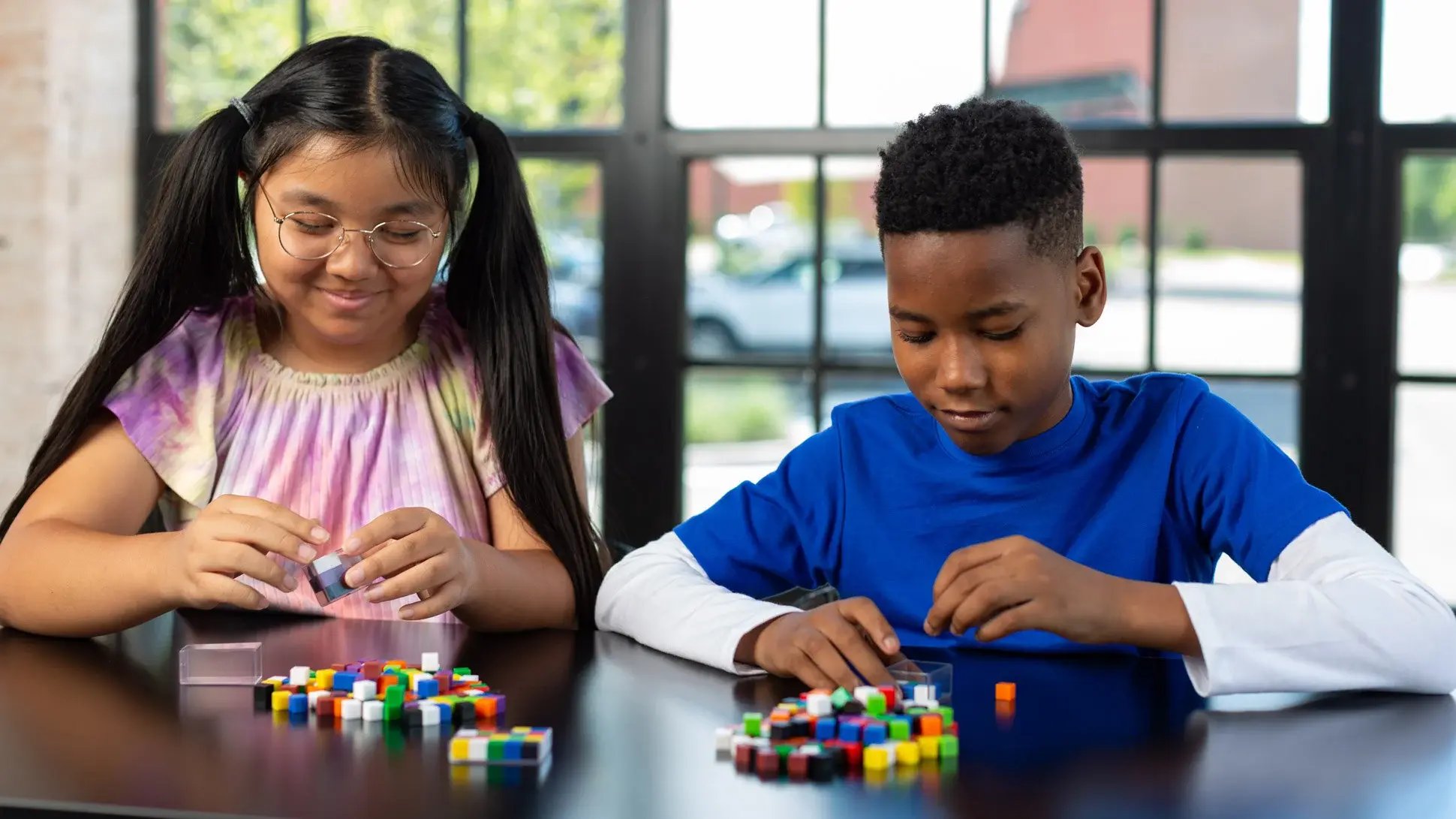 Two elementary students working with blocks at a classroom table.